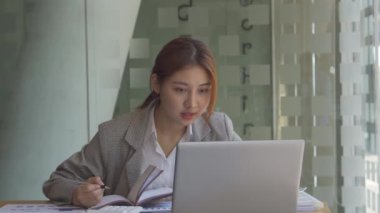 Finans muhasebesinde çalışan Asyalı bir kadın dizüstü bilgisayarla iş konsepti tablosunun hesaplama analizinde doküman çiziyor..
