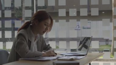 Finans muhasebesinde çalışan Asyalı bir kadın dizüstü bilgisayarla iş konsepti tablosunun hesaplama analizinde doküman çiziyor..