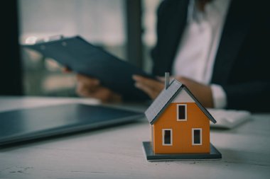 Bir emlakçı, sözleşmeyi imzaladıktan sonra müşterilerine faiz oranı sözleşmesi teklif eder. Ahşap bir masanın panosuna bir anlaşma imzalarken gayrimenkul ya da kiralama fikirleri.