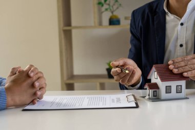 Emlakçılar müşterilerine ev satın alma, sigorta ya da emlak kredilerini görüşmek üzere sözleşmeler teklif ediyorlar. Ev satış temsilcileri ofiste yeni ev alıcılarıyla otururlar..