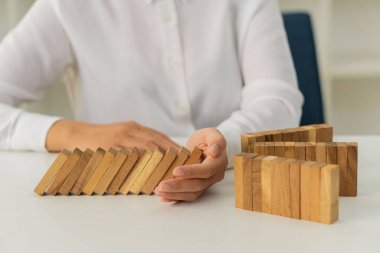 Domino 'nun mücadelesi yıkım ya da devam eden risk ve iş stratejisinin sonucudur. Kızın eli, üç geçidin arasındaki tahta bloğu Domino çizgisine düşmeden önce kapatır..