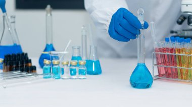 Bir kimya laboratuvarının arka planında laboratuvar camlarıyla dolu bir şişeyi tutan bilim adamının el aleti. Tıp ve Biyoteknoloji Laboratuarlarında Araştırma ve Geliştirme kavramları