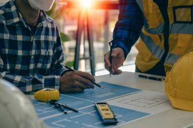 2 inşaat şantiyesi mühendisi inşaat alanında mühendislik objeleri interaktif ortaklar ve planlara işaret eden perde arkasında çalışıyorlar ve ofis tasarım projelerini çizmek için bir dizüstü bilgisayar kullanıyorlar..