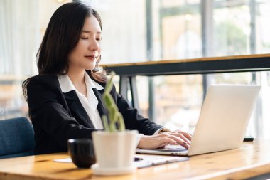 Asyalı iş kadını, kahve dükkanlarındaki müşterilerle dizüstü bilgisayar ve internet iletişimini kullanıyor. Laptopta oturan çekici kadın ve meşrubat restoranında akıllı telefon.