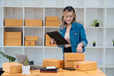 KOBİ küçük bir işletme kuruyor. Bir kadın girişimci kutuları hazırlamak için çevrimiçi siparişleri kabul etmek ve izlemek için kutular ve dizüstü bilgisayarlarla çalışıyor. Müşterilere satıyorum. Çevrimiçi KOBİ iş fikri.