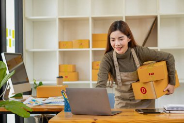 KOBİ küçük bir işletme kuruyor. Bir kadın girişimci kutuları hazırlamak için çevrimiçi siparişleri kabul etmek ve izlemek için kutular ve dizüstü bilgisayarlarla çalışıyor. Müşterilere satıyorum. Çevrimiçi KOBİ iş fikri.