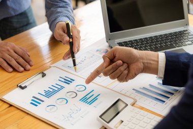 Belgelere işaret eden kalem tutan işletme ekibi mali verileri tartışıyor ve raporda iş danışmanlığı toplantıları ve yeni iş projeleri finans yatırım fikirleri üzerinde beyin fırtınası yapıyor