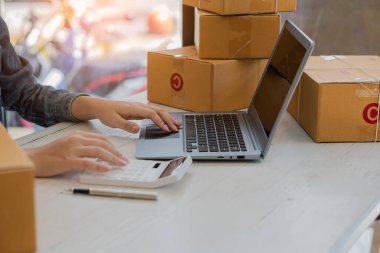 Küçük Girişimci, Girişim, KOBİ, Çalışmak için Genç Asyalılar ve Sevkiyat Konteynerleri çevrimiçi pazar yeri KOBİ 'si e-ticaret fikirlerini paketlediler ve evdeki dizüstü bilgisayarda müşteri siparişlerini kontrol ettiler.