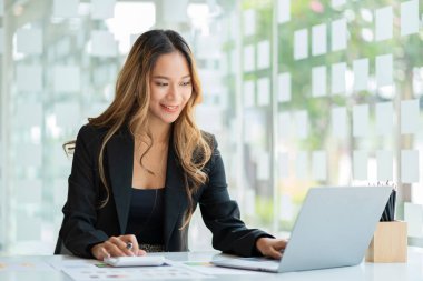 Güzel Asyalı iş kadını finansal harcamaları hesaplamak için dizüstü bilgisayarla çizelgeleri analiz ediyor. iş raporları ve muhasebe kavramı ile