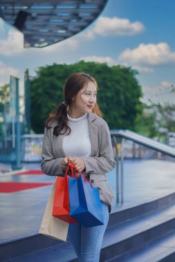 Gülümseyen, alışveriş merkezinde alışveriş yapan mutlu kız elinde renkli alışveriş torbalarıyla alışveriş merkezinde bulanık bir arka planda duruyor.