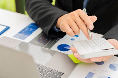 Asyalı işadamının eli, yatırım danışmanı grafiğini hesaplamak ve analiz etmek için kalem tutarken hesap makinesine basıyor ve veri hazırlıyor. ve bir dizüstü bilgisayarla maliyeti hesaplamak için denetçiler