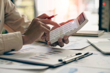 Asyalı işadamının eli, yatırım danışmanı grafiğini hesaplamak ve analiz etmek için kalem tutarken hesap makinesine basıyor ve veri hazırlıyor. ve bir dizüstü bilgisayarla maliyeti hesaplamak için denetçiler