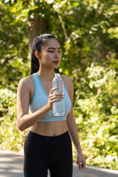アジアの女性はジョギング後に水を飲み 透明なペットボトルでスポーツをしたり 公園であなたを笑顔にしたり — ストック写真