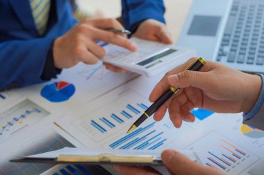 Modern bilgisayar dizüstü bilgisayarlarıyla ahşap bir masada konuşurken elinde kalem tutan iki iş adamının yakın çekimi. İş ekibinin analitik kavramlara ve stratejilerine yakın plan.