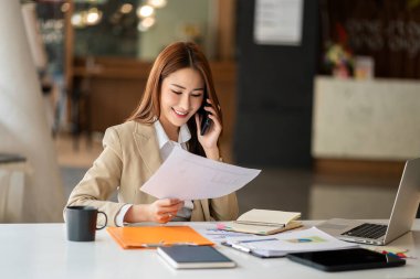 Gülümseyen Asyalı iş kadını dizüstü bilgisayar ve mali muhasebe konsebe ofisinde çalışıyor.