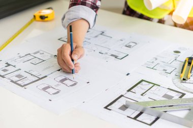 Genç mühendisler ve mimarlar, masanın üzerinde şapka ve ev tasarımı ve konseptleri için masa üstü araçları olan planlar tasarlıyor, planlıyor ve ölçüyor..