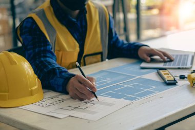 Genç mühendisler ve mimarlar, masanın üzerinde şapka ve ev tasarımı ve konseptleri için masa üstü araçları olan planlar tasarlıyor, planlıyor ve ölçüyor..