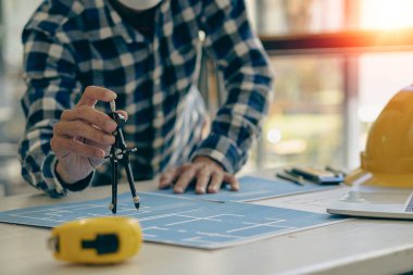 Genç mühendisler ve mimarlar, masanın üzerinde şapka ve ev tasarımı ve konseptleri için masa üstü araçları olan planlar tasarlıyor, planlıyor ve ölçüyor..