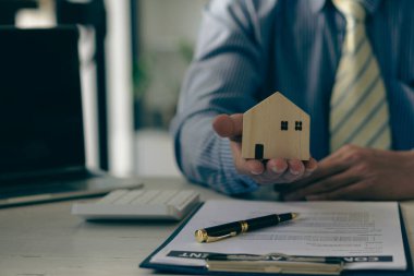 Emlak bürosunun satış temsilcileri, ev tasarımları ve hesap makineleriyle sözleşme belgeleriyle çalışırlar..