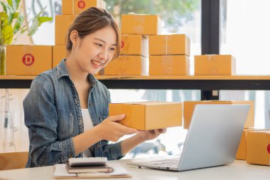 Küçük bir işletmenin portresi, KOBİ sahibi, bayan girişimci kutular ve dizüstü bilgisayarlar üzerinde çalışıyor, kutuları hazırlamak için online siparişleri işaretleyin. Müşterilere satıyorum. Çevrimiçi KOBİ iş fikri.