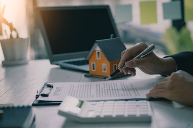 Bir işadamı ya da ev satış temsilcisi ofiste faiz, vergi ve kâr hesaplamak için sözleşme belgeleri ve hesap makineleriyle çalışır..