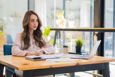 Gülümseyen Asyalı iş kadını şirket masasındaki dizüstü bilgisayarla finansal tabloları okuyarak pazar değişikliklerini gösteren grafikleri ve haritaları analiz ediyor..