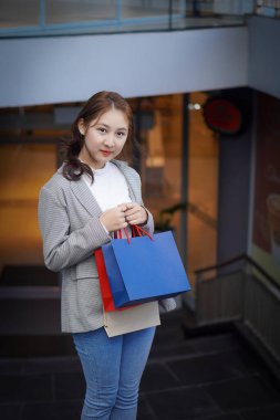 Genç bir kadın alışveriş çantalarını bir mağazanın önünde tutuyor, en sevdiği şeyleri almaktan mutluluk duyuyor..