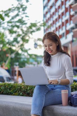 Dışarıda dizüstü bilgisayarda çalışan, konseptleri inceleyen, halka açık alanda çalışan genç Asyalı tatlı bir kız öğrenci..