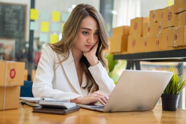 İş yerinde kutu ve dizüstü bilgisayarla çalışan Asyalı bir kadın, küçük işletme sahibi Girişimcilik, küçük işletme, KOBİ veya serbest internet üzerinden ve dağıtım fikirleri başlatıyor.