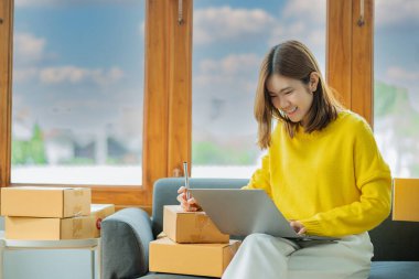 İş yerinde kutu ve dizüstü bilgisayarla çalışan Asyalı bir kadın, küçük işletme sahibi Girişimcilik, küçük işletme, KOBİ veya serbest internet üzerinden ve dağıtım fikirleri başlatıyor.