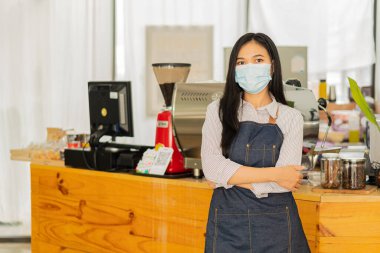 Önlüklü genç bir Asyalı barista bir işletme sahibinin başlangıç konseptinin önünde duruyor. KOBİ kafe kasiyerini yöneten başarılı kadın.