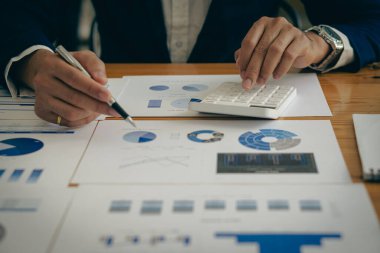 Bir iş adamı, fiyat tahminini dizüstü bilgisayarla hesaplamak için hesap makinesine basar. Muhasebeciler aylık mali raporlar ya da şirket kârlarını masalarında yapıyorlar. ve evden çalışma kavramı