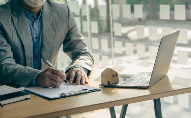 Emlak bürosu işadamı, faiz oranları, ev satın alma ve sigorta fikirleri olan müşterilere sözleşme belgeleriyle çalışıyor..