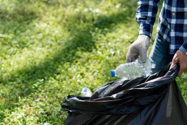 Çöp toplayıcısının eli. Yerde kaynayan boş plastik su şişesi. Yerden plastik şişeleri toplamaya odaklan. Çevre kavramı.