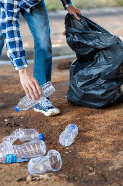 Çöp toplayıcısının eli. Yerde kaynayan boş plastik su şişesi. Yerden plastik şişeleri toplamaya odaklan. Çevre kavramı.