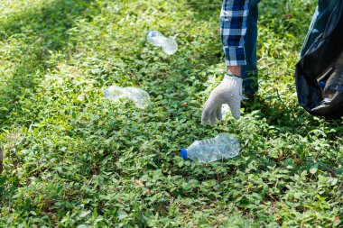 Çöp toplayıcısının eli. Yerde kaynayan boş plastik su şişesi. Yerden plastik şişeleri toplamaya odaklan. Çevre kavramı.