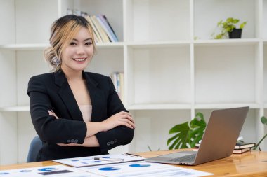 Güzel Asyalı iş kadını hesap makinesi kullanarak analiz çizelgesi, ofiste elinde kağıtlar ve elinde kalemle modern ev stüdyosundaki sandalyede oturuyor. Cep telefonu işçisi müşterilerle bağlantı kuruyor