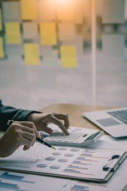 İş adamları hesap makineleri ve iş grafikleri üzerinde çalışıyorlar. Ofisteki finansal piyasa analistleri ellerinde grafik ve diyagramlarla tahta masalarda oturuyorlar.
