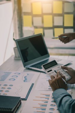 İş adamları hesap makineleri ve iş grafikleri üzerinde çalışıyorlar. Ofisteki finansal piyasa analistleri ellerinde grafik ve diyagramlarla tahta masalarda oturuyorlar.