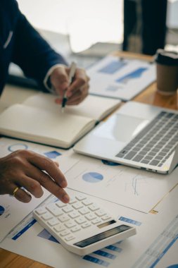 İş adamları hesap makineleri ve iş grafikleri üzerinde çalışıyorlar. Ofisteki finansal piyasa analistleri ellerinde grafik ve diyagramlarla tahta masalarda oturuyorlar.