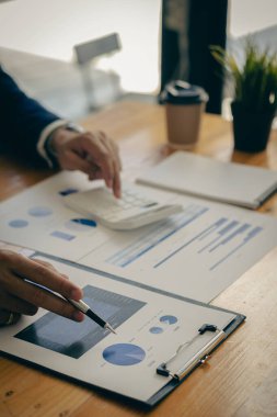 İş adamları hesap makineleri ve iş grafikleri üzerinde çalışıyorlar. Ofisteki finansal piyasa analistleri ellerinde grafik ve diyagramlarla tahta masalarda oturuyorlar.