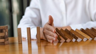 Kızın eli tahta blok dominolarını durduruyor. Ardışık düşüş etkisi veya riskler, stratejiler ve işletmeler için başarılı müdahale fikirleri.