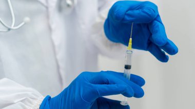 Koruyucu eldivenlerle bir doktorun elinin yakın çekimi, Coronavirus aşısı ile bir şırınga tutan eller, ve yontulmuş adam komplo teorisi.