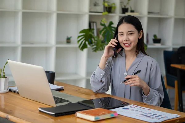 Asyalı iş kadını, masada duran çalışma grafiği belgesini hesaplamak için istatistiksel analizi hesaplayan bir hesap makinesiyle masada iş görüşmesi yapmak için akıllı telefon kullanıyor.