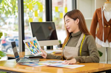 Asyalı terzi tasarımcı terzisinde kıyafet tasarlıyor. Güzel kız, atölye ve iş fikrindeki yeni el yapımı elbiseyi başarıyla yaptıktan sonra gülümsüyor..