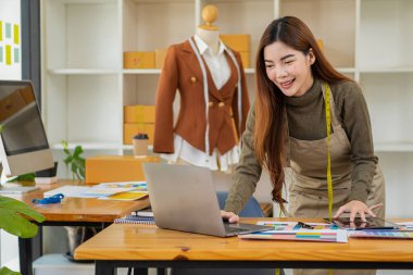 Asyalı terzi tasarımcı terzisinde kıyafet tasarlıyor. Güzel kız, atölye ve iş fikrindeki yeni el yapımı elbiseyi başarıyla yaptıktan sonra gülümsüyor..