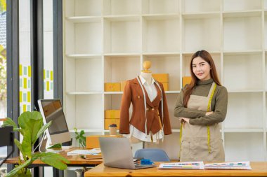 Asyalı terzi tasarımcı terzisinde kıyafet tasarlıyor. Güzel kız, atölye ve iş fikrindeki yeni el yapımı elbiseyi başarıyla yaptıktan sonra gülümsüyor..