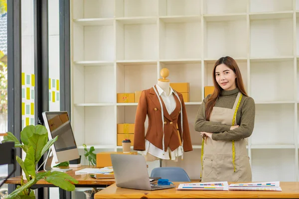 Asyalı terzi tasarımcı terzisinde kıyafet tasarlıyor. Güzel kız, atölye ve iş fikrindeki yeni el yapımı elbiseyi başarıyla yaptıktan sonra gülümsüyor..