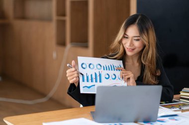 Güzel Asyalı iş kadını dizüstü bilgisayar hesap makinesi ve çek defteri kullanarak çizelgeleri analiz ediyor.