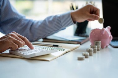 Tasarruf, para, sigorta, emekli maaşı, emeklilik ve insanların kavramları. Bir kavanozda bozuk para ve hesap makinesiyle masanın üstünde duran bir gencin el resmi.